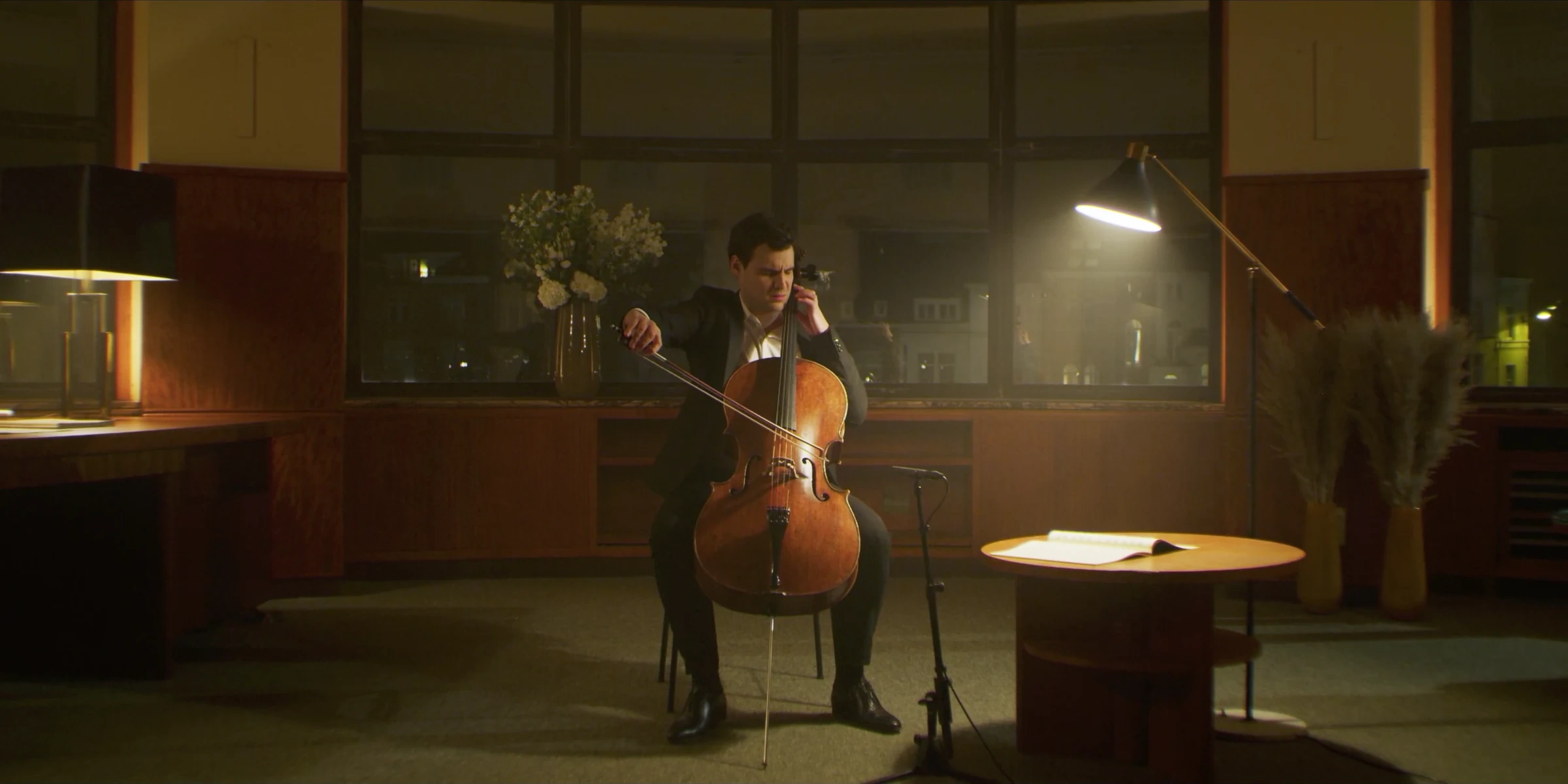 Cellist performing beside a lamp and an open score