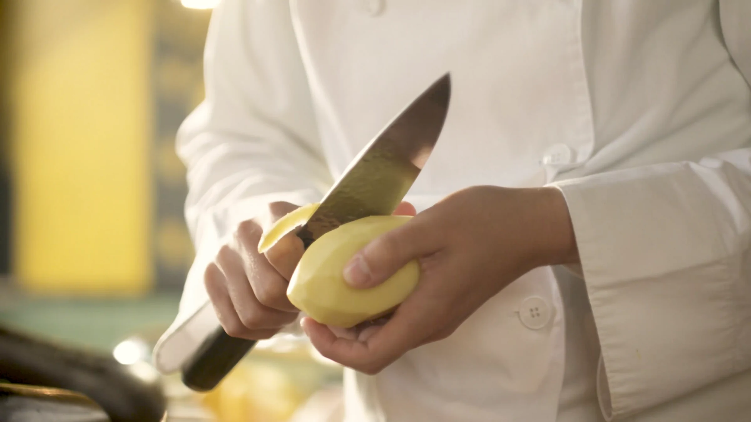 Chef peeling a potato in warm light